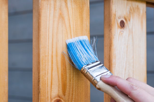a paintbrush applying wood stain to a deck