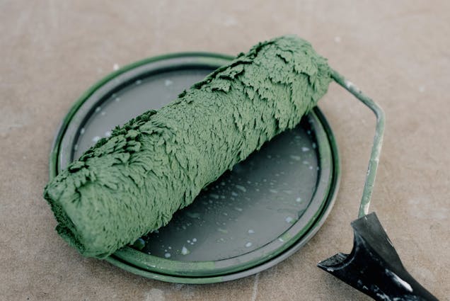 a green paint roller resting on a paint can lid