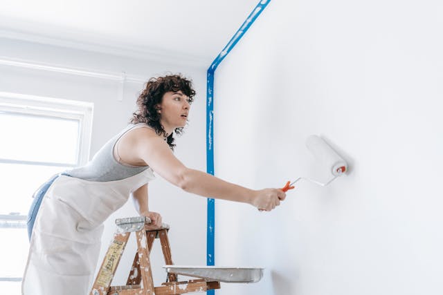 person in a smock painting a wall white