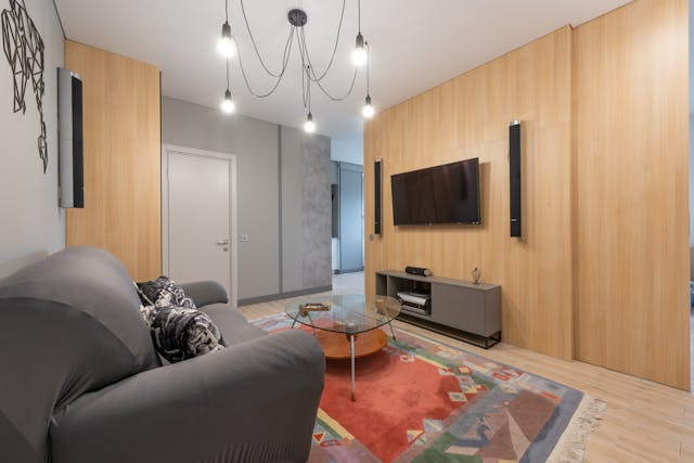 a wooden-paneled loving room with a colourful rug and a grey couch